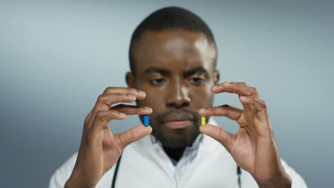 Close-up-of-the-young-African-american-doctor-holding-two-pills-in-hands---yellow-and-blue---and-looking-at-them.
